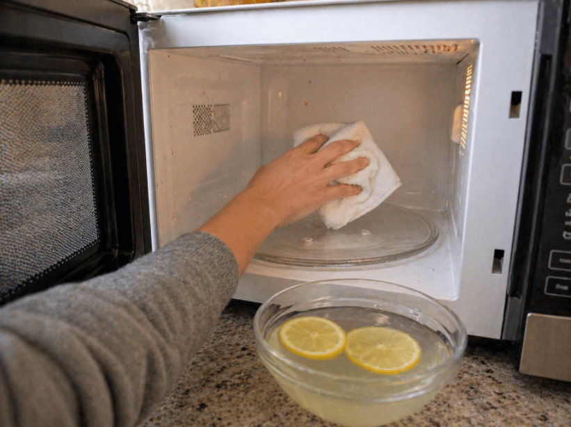 person wiping the inside of a microwave with a towel while a bowl of lemon water sits nearby