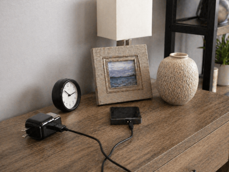 bedroom shelf with common hidden camera hiding spots including a clock, charger, picture frame, and decorative vase